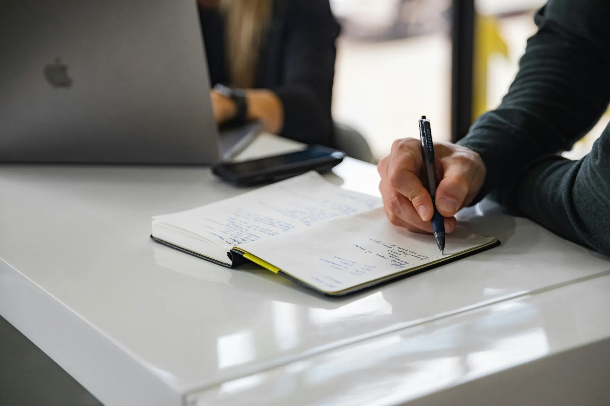 Handschriftliche Notizen auf einem Schreibtisch neben Laptop und Smartphone