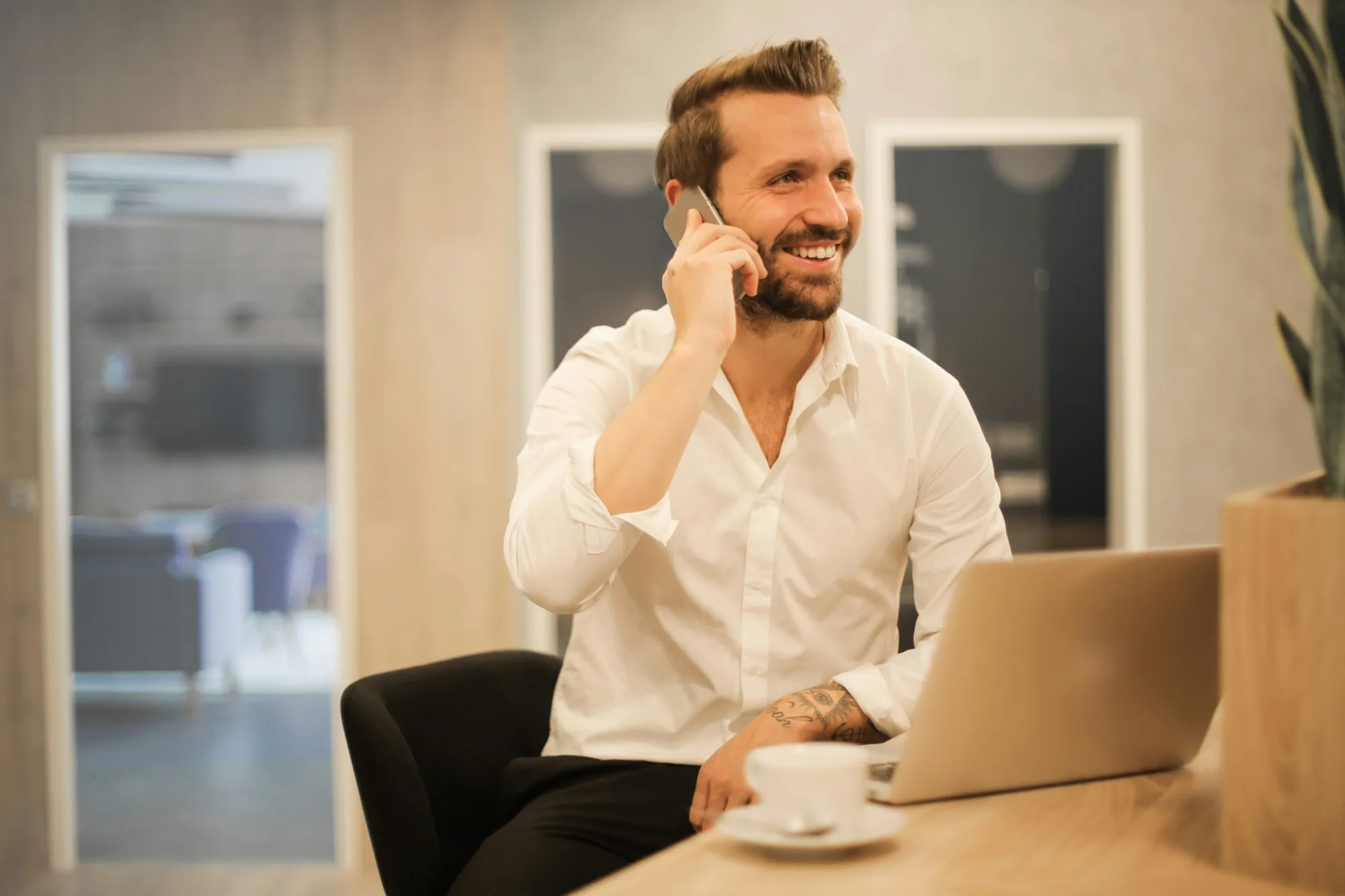 Ein Mann telefoniert lächelnd an seinem Arbeitsplatz mit Laptop
